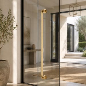 May include: A polished gold door pull handle, with a curved design, is fixed to a glass door. The handle has a smooth, cylindrical form with decorative, rounded ends. The door is part of a contemporary entrance, with a view of an outdoor space visible through the glass.