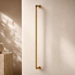 May include: A long, gold-coloured grab bar fixed to a cream-coloured wall. The bar has curved ends and a sleek, polished surface. The design is minimalist and contemporary, ideal for bathrooms or for accessibility. The bar's length is approximately 70 cm.