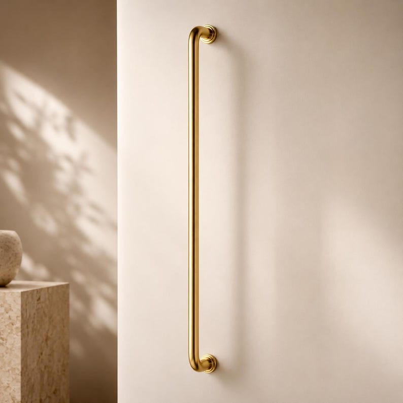 May include: A long, gold-coloured grab bar fixed to a cream-coloured wall. The bar has curved ends and a sleek, polished surface. The design is minimalist and contemporary, ideal for bathrooms or for accessibility. The bar's length is approximately 70 cm.