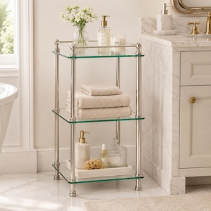 Könnte beinhalten: Ein dreistufiges Badezimmerregal aus Glas und Chrom. Das oberste Regal enthält eine Vase mit weißen Blumen, einen Seifenspender und eine Kerze. Das mittlere Regal hat gefaltete beige Handtücher. Das untere Regal zeigt einen Seifenspender, ein Tablett mit einem Schwamm und anderes Badezubehör.