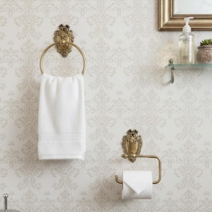 May include: Bathroom accessories set in a gold finish. Includes a towel ring with a white towel, a toilet paper holder, and a decorative wall mount. The wallpaper has a light floral pattern.