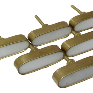 May include: Six brass cabinet knobs with a white, oval-shaped center. The knobs have a simple, elegant design, perfect for adding a touch of sophistication to furniture or cabinetry. Each knob has a stem for easy installation.