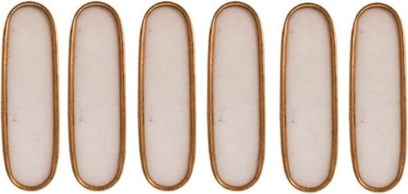 May include: Six elongated, oval-shaped decorative elements. Each has a white, opaque center framed by a thin, copper-colored metal border. The objects are arranged in a horizontal row, showcasing their uniform design and finish.