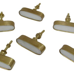 May include: Six brass cabinet knobs with a white, oval-shaped center. The knobs have a simple, elegant design, perfect for adding a touch of sophistication to any furniture piece. The knobs are shown against a white background.