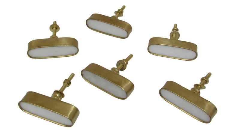 May include: Six brass cabinet knobs with a white, oval-shaped center. The knobs have a simple, elegant design, perfect for adding a touch of sophistication to any furniture piece. The knobs are shown against a white background.