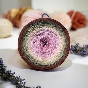 May include: A round cake of gradient yarn featuring a color transition from a deep brown outer edge to a soft cream, transitioning into a muted sage green, and finally a vibrant pink center. The yarn is tightly wound in a circular pattern.