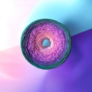 May include: A circular cake of yarn featuring a gradient color transition. The outer edge is a deep teal, shifting inward through shades of purple and magenta, and culminating in a light pink center with a hollow core, viewed from directly above.