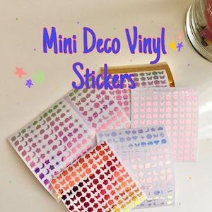 May include: Multiple sheets of mini vinyl stickers featuring holographic and gradient finishes in shapes like butterflies, stars, moons, and hearts. The text "Mini Deco Vinyl Stickers" is printed in blue and purple at the top of the image.