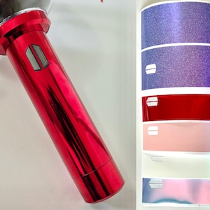 May include: A red metallic light stick with a silver top and a logo. Beside it are colorful stickers with glitter and the same logo in different colors, including blue, red, and pink.