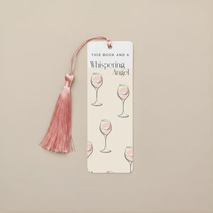 May include: A cream-coloured bookmark with a pink tassel. The bookmark features illustrations of wine glasses. Text on the bookmark reads "THIS BOOK AND A Whispering Angel."