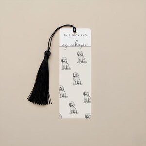 May include: A cream bookmark with a repeating pattern of Cockapoo dog illustrations. The bookmark has the text "THIS BOOK AND my cockapoo" and is attached to a black tassel.