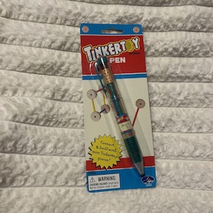以下が含まれることがあります： Tinkertoyブランドのペンがパッケージに入っています。ペンはマルチカラーで、緑、シルバー、透明のバレルです。パッケージは青と赤で、「Tinkertoy Pen」の文字と小さな部品に関する警告があります。