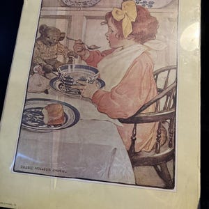 May include: A vintage-style print titled Breakfast with Teddy by Jessie Wilcox Smith, depicting a child with a yellow hair bow eating from a blue and white bowl while seated at a table with a teddy bear. The print includes text at the bottom.