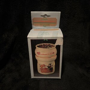May include: A ceramic Christmas candle holder in a box. The candle holder is off-white with a teddy bear and elf design. The box reads "Christmas is Love" and "Create Holiday Spirit in Your Home."