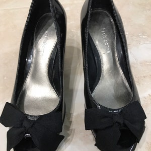 May include: Black patent leather peep-toe heels with a black bow on the front. The shoes are labeled "Liz Claiborne".