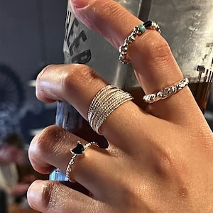 May include: A hand wearing several gold rings, including a ring with a black heart-shaped stone.