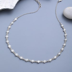May include: A silver chain necklace with small white pearl accents. The necklace has a lobster clasp closure.