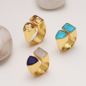 May include: Three gold-colored rings with different gemstone combinations. One ring features a triangular and rectangular light brown stone. Another has a triangular and rectangular turquoise stone. The third ring has a triangular dark blue and rectangular light gray stone.