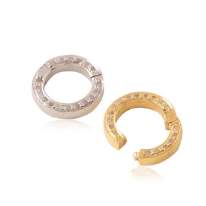 K&ouml;nnte beinhalten: Zwei Ringe aus Silber und Gold mit einer Reihe kleiner Diamanten am Rand. Die Ringe sind offen und haben einen Scharnierverschluss.