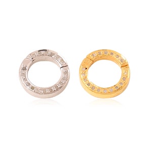 K&ouml;nnte beinhalten: Zwei runde Schmuckverschl&uuml;sse, einer in Silber und einer in Gold, mit einer Reihe kleiner Diamanten am Rand.