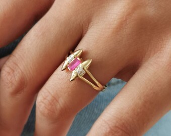 May include: Gold ring with a pink gemstone and clear stones. The ring has a pointed design.