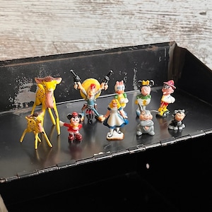 May include: A black metal box with a hinged lid. The lid is open and there are small figurines of various characters inside. The figurines are made of painted metal and include a deer, a cowboy, a woman in a dress, a witch, and a few others.