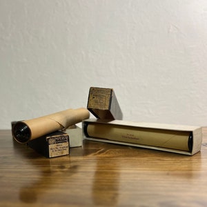 May include: Three vintage music rolls in their original boxes. The rolls are made of paper and are rolled up. The boxes are made of cardboard and have black lettering on a white background. The boxes are labeled with the titles of the music rolls: "She's The Sweetheart Of The Old Home Town", "No. 3128 "What The World Needs!" and "Imperial Record Company".