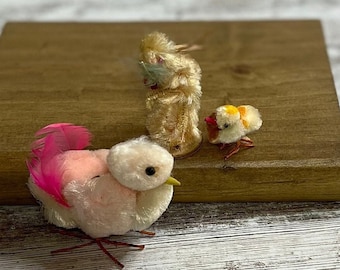 May include: Three small, handmade felt birds. One is pink with a pink tail, one is yellow with a yellow tail, and one is cream with a green tail.