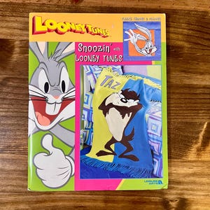 May include: A Looney Tunes Snoozin' fleece throw and pillow set. The box features Bugs Bunny and Taz, with the words "Looney Tunes" in yellow and red. The throw has a blue, yellow, and green design with Taz.
