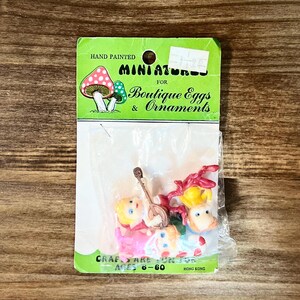 May include: A package of hand-painted miniatures for boutique eggs and ornaments. The package includes small figurines of musicians and a musical instrument. The package is green and has the text "HAND PAINTED MINIATURES FOR Boutique Eggs & Ornaments".