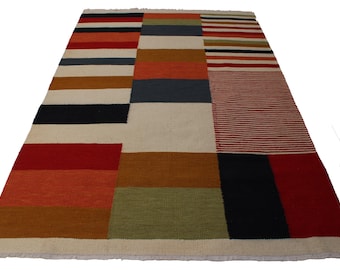 May include: A rectangular area rug featuring a patchwork design of horizontal and vertical stripes in various colors including red, orange, dark blue, olive green, and cream. The rug has a woven texture and a short fringe along the edges.
