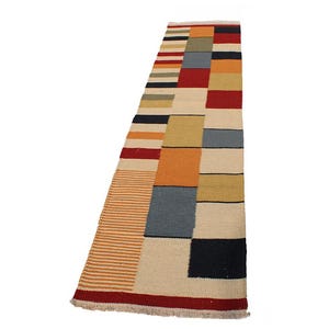 May include: A rectangular rug with a geometric pattern. The rug features a combination of colors, including beige, red, orange, yellow, blue, and black. The design includes stripes and rectangular blocks. The rug has a fringed edge.