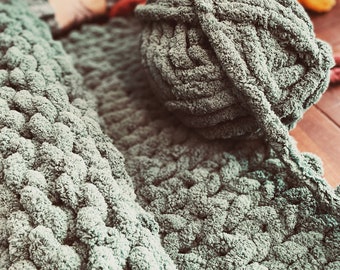 Könnte beinhalten: Nahaufnahme einer dicken, grünen Strickdecke aus dickem Garn. Die Decke ist mit einem einfachen Stichmuster gearbeitet und hat eine weiche, flauschige Textur.