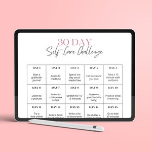May include: A digital tablet displaying a 30-day self-care challenge with daily activities, such as starting a gratitude journal, learning to meditate, and taking a walk outdoors. The tablet is on a pink surface with a stylus next to it.