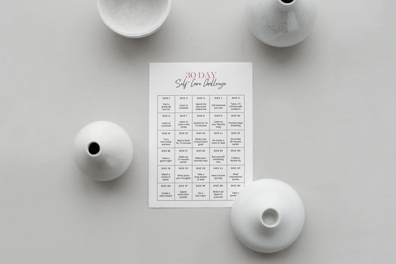 May include: A printable 30-day self-care challenge with a grid of daily activities. The grid is printed on white paper and has a pink title. The image also shows four white ceramic vases.