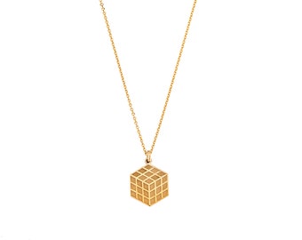May include: A gold necklace with a geometric cube pendant. The cube has a grid pattern.