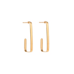 May include: A pair of gold-colored, rectangular hoop earrings. Each earring has a straight, vertical bar that curves at the bottom to form a hook. The earrings are displayed against a white background.