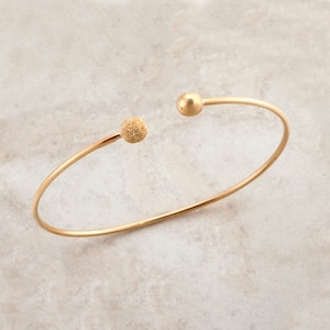 May include: A gold bangle bracelet with two textured round balls at the ends.