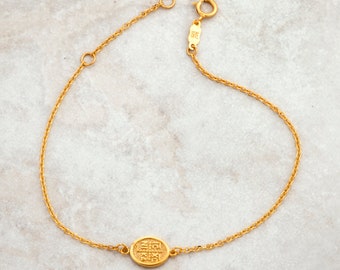 May include: A gold chain bracelet with a small round charm featuring an inscription in a foreign language.