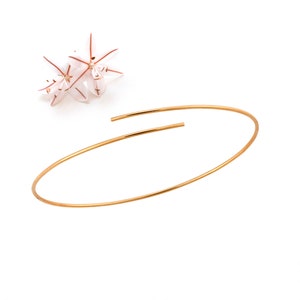 Può includere: Un braccialetto semplice in oro con un design aperto delicato. Il braccialetto è realizzato con un filo sottile e rotondo e ha una forma leggermente curva.