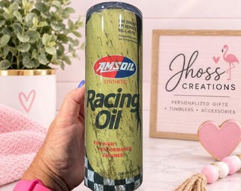 May include: A cylindrical tumbler with a yellow and black distressed finish, featuring the Amsoil Racing Oil logo, the text For High Performance Engines, and a black and white checkered pattern at the base, with a clear lid on top.
