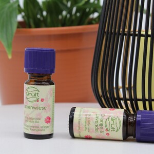 May include: Two small glass bottles with purple lids and labels that say "Gr&uuml;lt" and "Orange & Lavendel" in pink and green lettering. The bottles are sitting on a white surface.