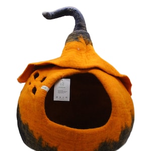 Może przedstawiać: Pomarańczowe i czarne filcowe legowisko dla kota w kształcie dyni z czarnym filcowym trzonkiem. Legowisko ma duży otw&oacute;r, przez kt&oacute;ry kot może wejść, oraz małą metkę z tekstem "Live Sustainably" z boku.