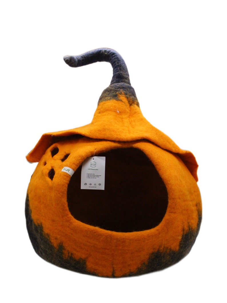 Może przedstawiać: Pomarańczowe i czarne filcowe legowisko dla kota w kształcie dyni z czarnym filcowym trzonkiem. Legowisko ma duży otw&oacute;r, przez kt&oacute;ry kot może wejść, oraz małą metkę z tekstem "Live Sustainably" z boku.