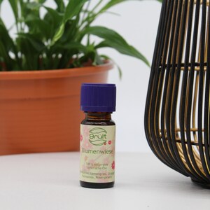 May include: A small brown glass bottle with a purple cap. The bottle is labeled "Grult Blumenwiese 100% nat&uuml;rliche &auml;therische &Ouml;le  Zitronenverbene, Orange,  Mandarine, Rosenranke"