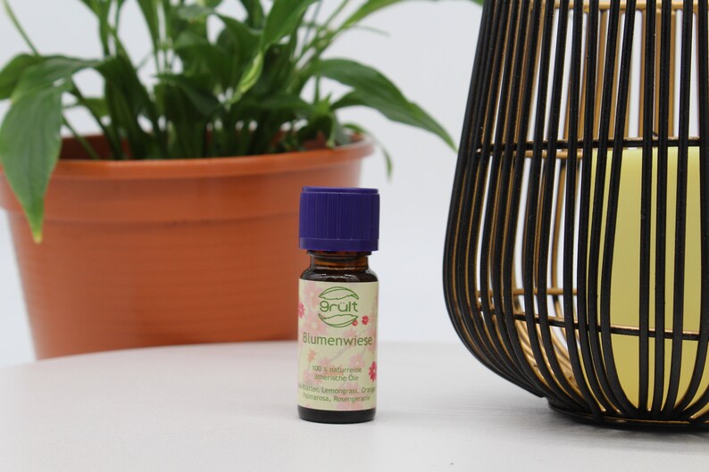 May include: A small brown glass bottle with a purple cap. The bottle is labeled "Grult Blumenwiese 100% nat&uuml;rliche &auml;therische &Ouml;le  Zitronenverbene, Orange,  Mandarine, Rosenranke"