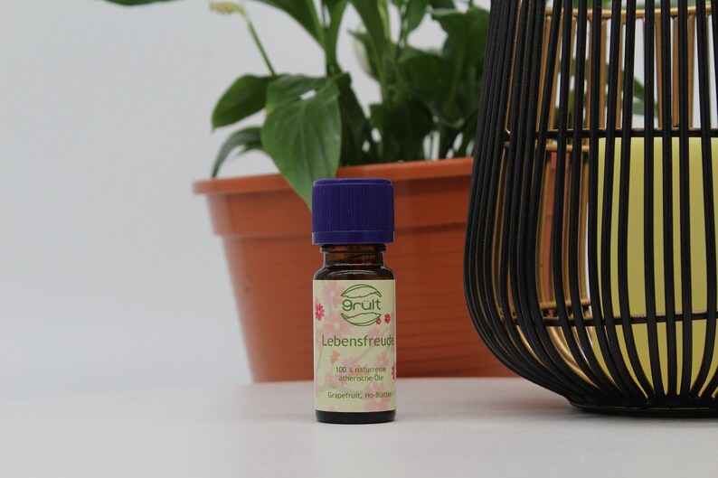 May include: A small brown glass bottle with a purple cap. The bottle is labeled "Gr&uuml;t Lebensfreude 100% nat&uuml;rliche &auml;therische &Ouml;le Grapefruit, Ho-Wood".