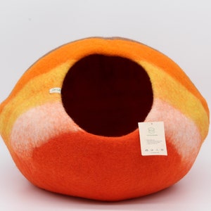 Może przedstawiać: Kojec dla kota z filcu w kolorze pomarańczowym, ż&oacute;łtym i białym w kształcie kopuły. Kojec ma okrągły otw&oacute;r, przez kt&oacute;ry kot może wejść.