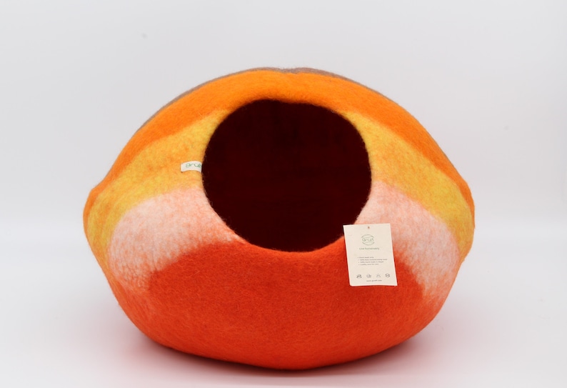 Może przedstawiać: Kojec dla kota z filcu w kolorze pomarańczowym, ż&oacute;łtym i białym w kształcie kopuły. Kojec ma okrągły otw&oacute;r, przez kt&oacute;ry kot może wejść.