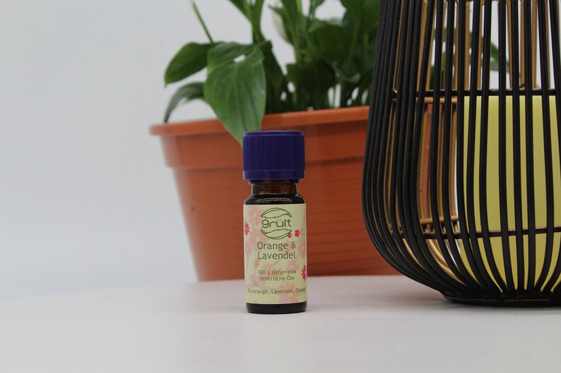 May include: A small, brown glass bottle with a purple cap. The bottle is labeled "gr&uuml;t Orange & Lavendel 100% nat&uuml;rliche &auml;therische &Ouml;le Orange, Lavendel, Orange"